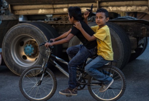  Dois meninos em uma bicicleta no centro da Cidade da Guatemala, o garupa com um revólver de brinquedo na mão. As armas são parte cotidiana nas cidades deste país centro-americano. Foto: Ximena Natera/Pie de Página